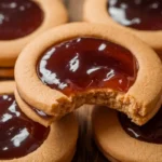 Freshly baked peanut butter and jelly cookies on a wooden table with a glass of milk.